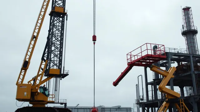 Crawler crane and boom lift working alongside steel structures on an oil and gas construction site